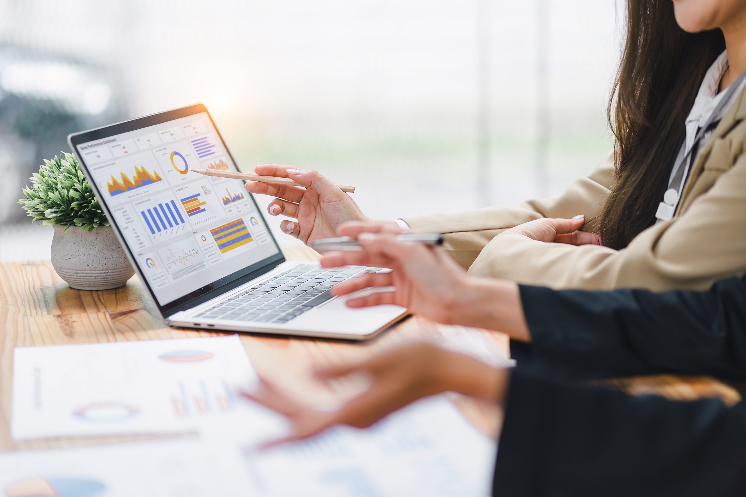 Two professional analyzing data graphs, charts on laptop display at a modern workspace.