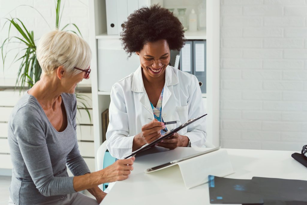 A female doctor sits at her desk and chats to an elderly female patient while looking at her test results