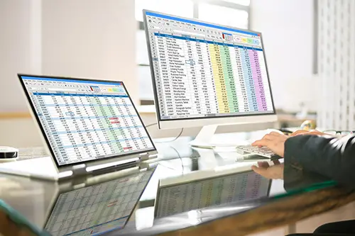 Medical data Spreadsheets on two monitors being analyzed by an employee