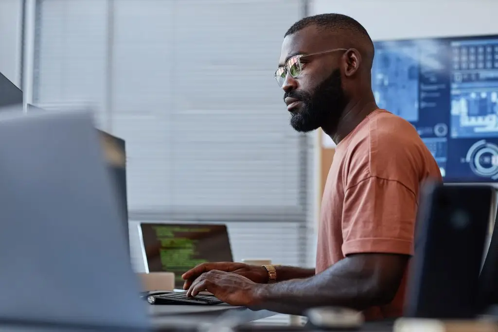 Side view portrait of black office employee using computer in high technology office, data systems