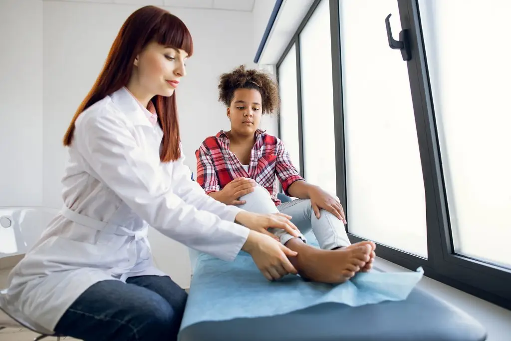 Female doctor orthopedist, examining foot of a teen girl in clinic.